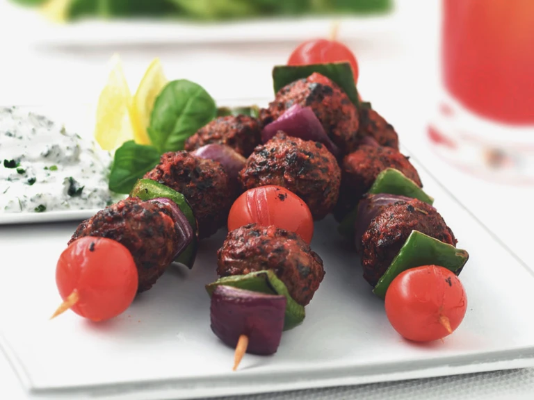 Three kebabs stacked with Quorn Meatballs, cherry tomatoes, green peppers, and red onions with a small dish of yogurt sauce on the side.