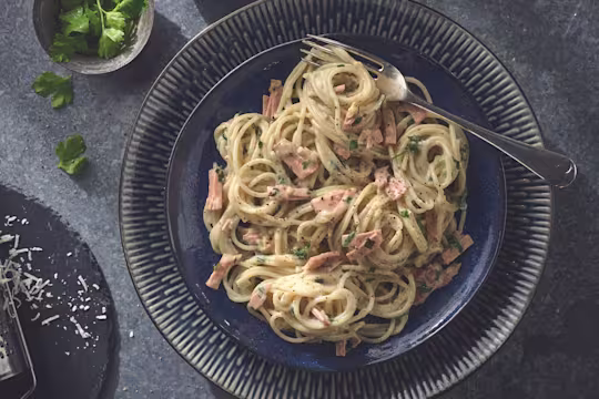 Vegan carbonara made with Quorn Smoky Vegan Ham garnished with chopped parsley served on a plate with a fork
