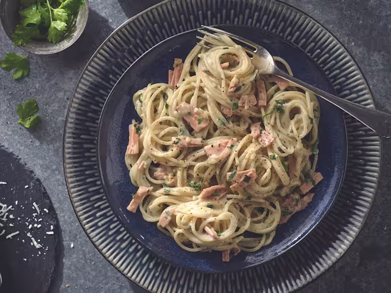 Vegan carbonara made with Quorn Smoky Vegan Ham garnished with chopped parsley served on a plate with a fork