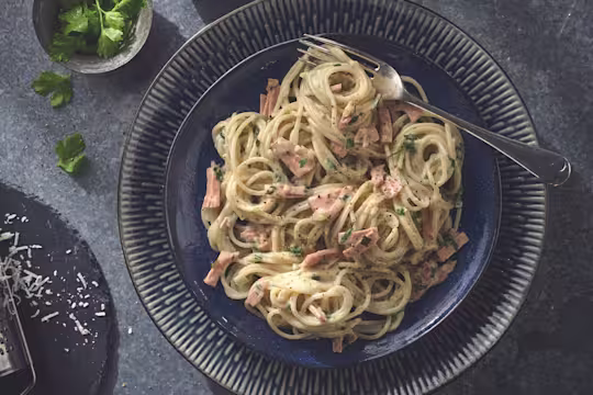 Vegan carbonara made with Quorn Smoky Vegan Ham garnished with chopped parsley served on a plate with a fork
