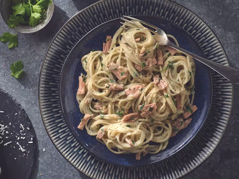 Vegan carbonara made with Quorn Smoky Vegan Ham garnished with chopped parsley served on a plate with a fork