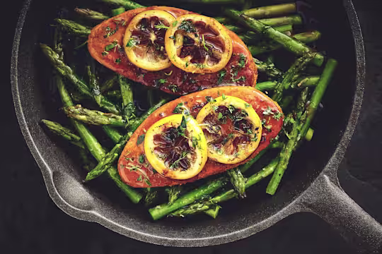 Quorn Fillets topped with lemon slices atop a bed of asparagus in a cast iron skillet.