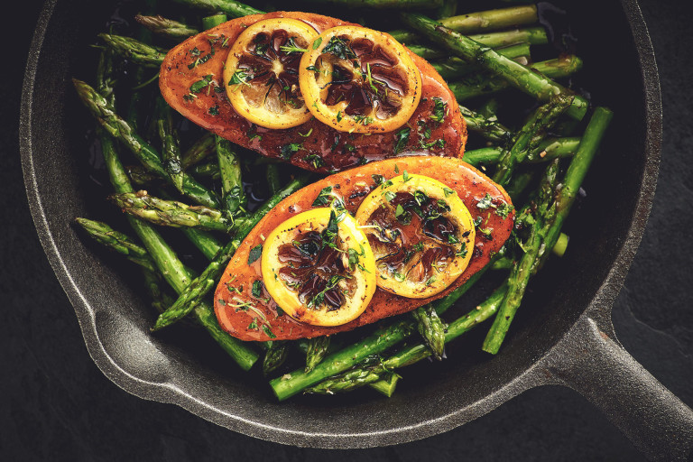 Quorn Fillets topped with lemon slices atop a bed of asparagus in a cast iron skillet.