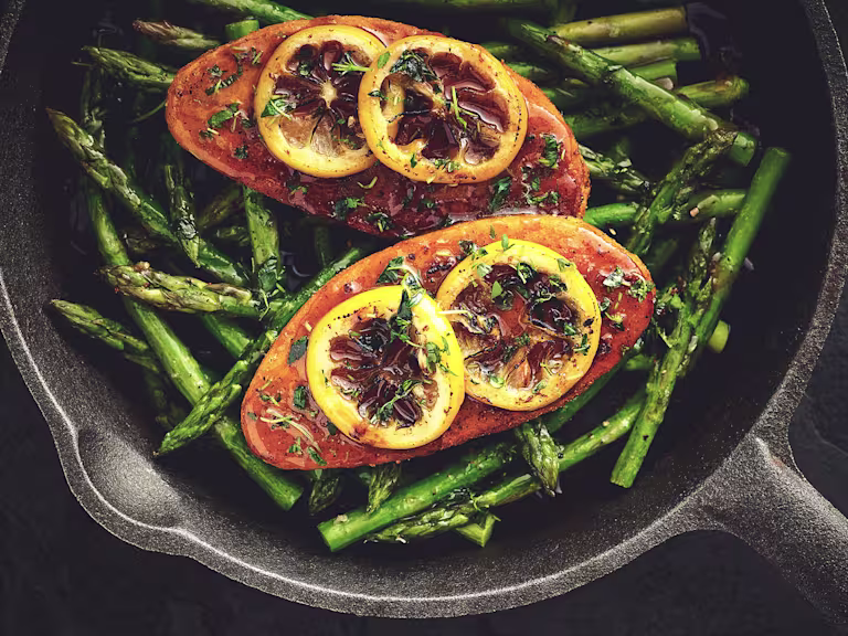 Quorn Fillets topped with lemon slices atop a bed of asparagus in a cast iron skillet.