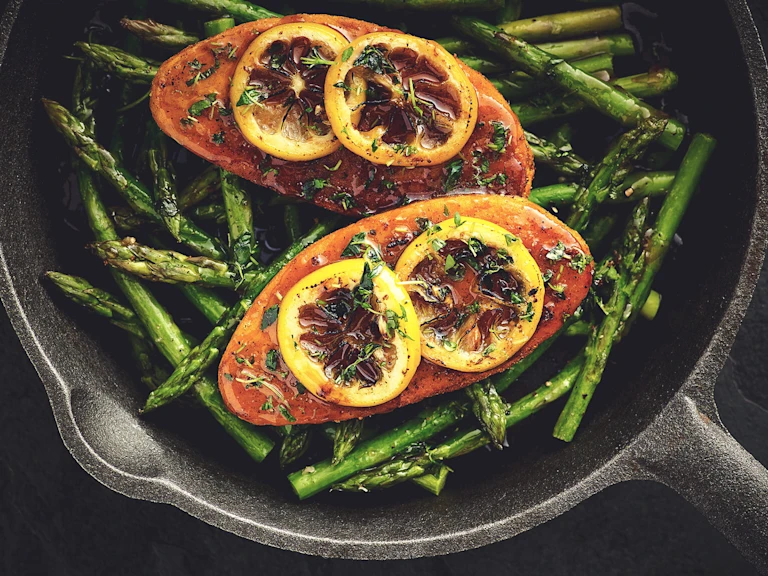Quorn Fillets topped with lemon slices atop a bed of asparagus in a cast iron skillet.