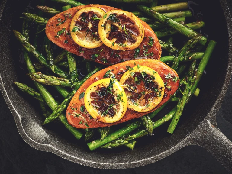 Quorn Fillets topped with lemon slices atop a bed of asparagus in a cast iron skillet.