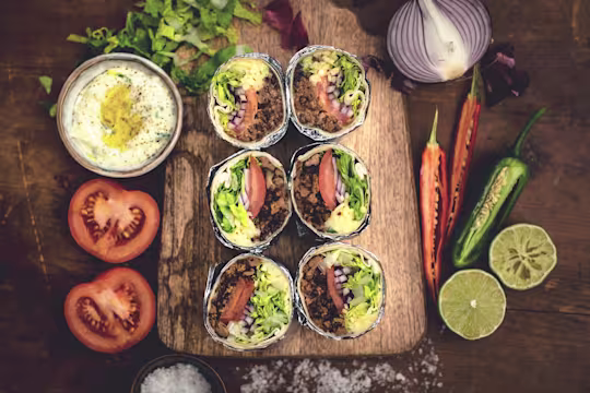 A serving slab with 6 Quick & Easy Quorn Mince Burritos served with fresh lime, chilli, tomato, red onion & veggie mayonnaise
