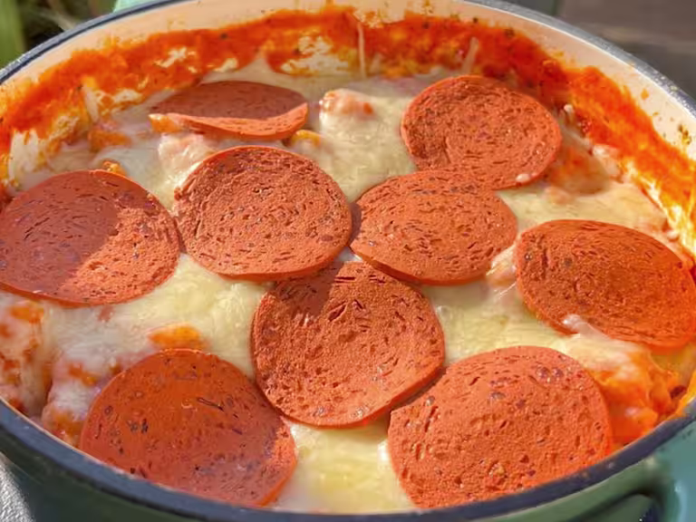 Cheese and Quorn Pepperoni topped pizza orzo in a casserole dish on a table.