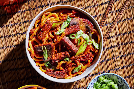 A bowl of vegetarian bulgogi noodles made with Quorn Steak Strips and udon noodles topped with scallions with a bowl of quick-pickled vegetables on the side.