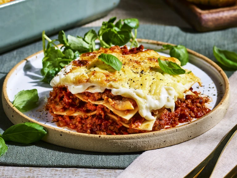 A slice of meat-free lasagne served alongside greens on a brown dish.
