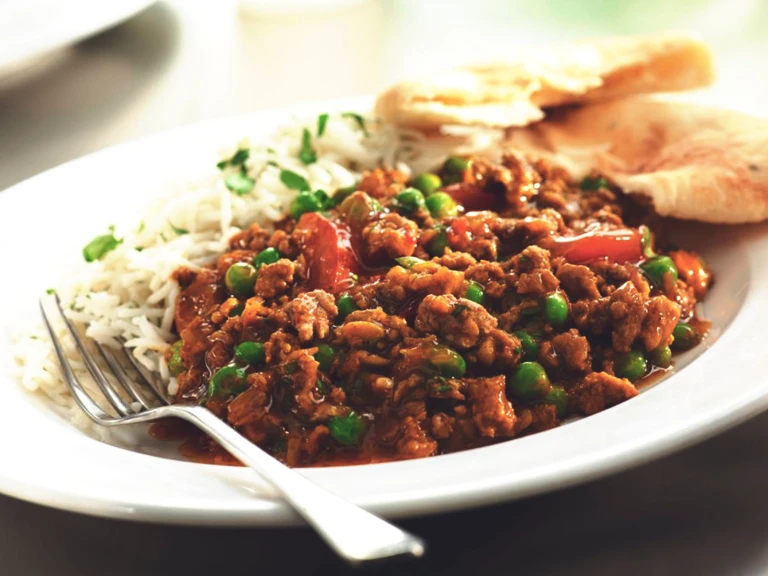 Keema curry made with vegetarian Quorn Mince, peas and red pepper served next to rice in a bowl with naan bread on the side