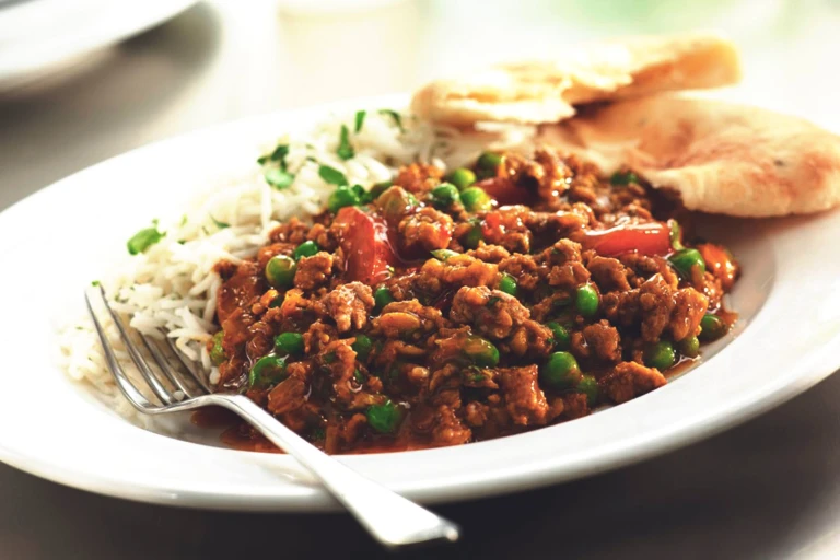 Keema curry with peas served alongside rice and flatbread.