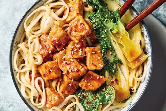 Yakisoba med Quorn Bitar och nudlar, grönsaker och ätpinnar, i en vit skål mot en blå bakgrund.