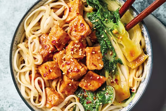 Yakisoba med Quorn Bitar och nudlar, grönsaker och ätpinnar, i en vit skål mot en blå bakgrund.