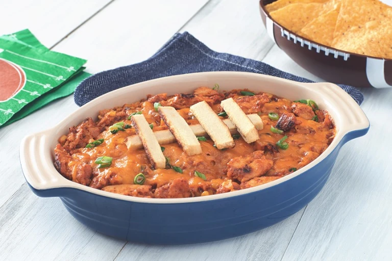 A blue oblong-shaped dish filled with bbq chickenless dip with Quorn Fillet slices arranged on top to make the dish resemble a football.