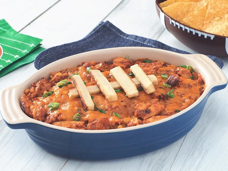 A blue oblong-shaped dish filled with bbq chickenless dip with Quorn Fillet slices arranged on top to make the dish resemble a football.