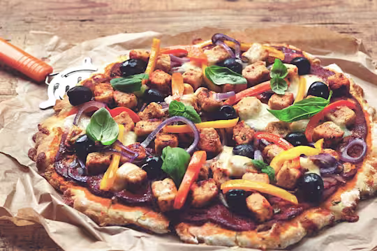 Gluten free pizza recipe made with Quorn Pieces and mixed veggies, served on baking paper with a pizza wheel on the side