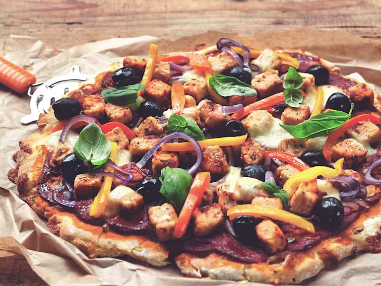 Gluten free pizza recipe made with Quorn Pieces and mixed veggies, served on baking paper with a pizza wheel on the side