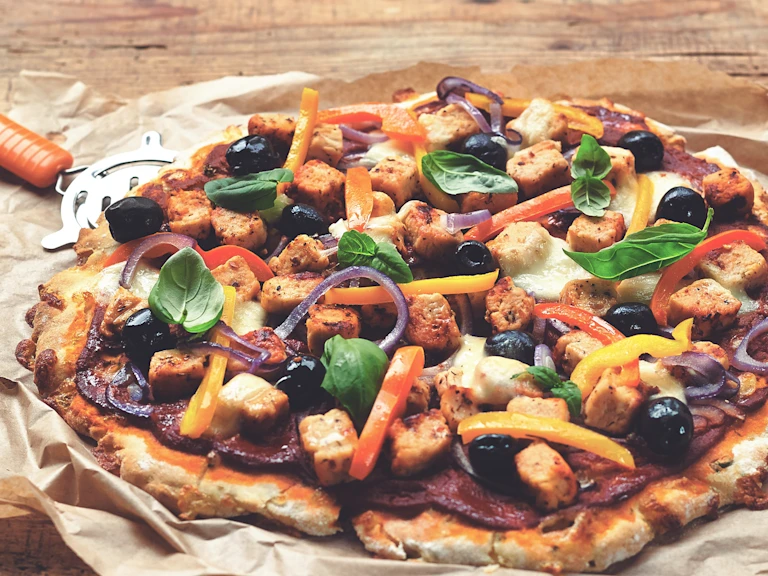 Gluten free pizza recipe made with Quorn Pieces and mixed veggies, served on baking paper with a pizza wheel on the side