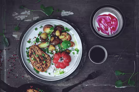 Quorn Vegetarian Peppered Steak, roast potatoes and tomato served on a plate dressed with salad leaves and a side of yoghurt
