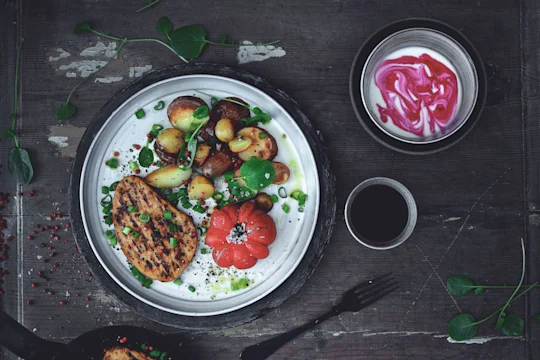 Quorn Vegetarian Peppered Steak, roast potatoes and tomato served on a plate dressed with salad leaves and a side of yoghurt