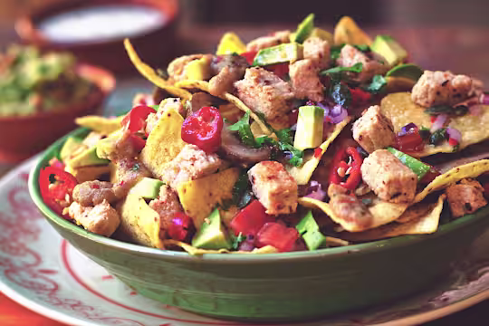 Nachos topped with salsa, mushrooms, red onions, nacho sauce, avocado, and Quorn ChiQin Pieces in a green bowl.