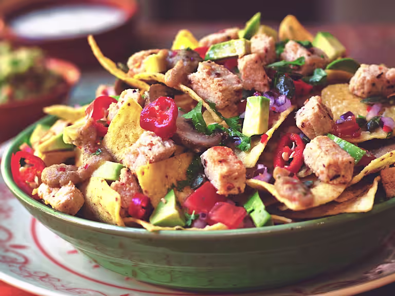 Nachos topped with salsa, mushrooms, red onions, nacho sauce, avocado, and Quorn ChiQin Pieces in a green bowl.