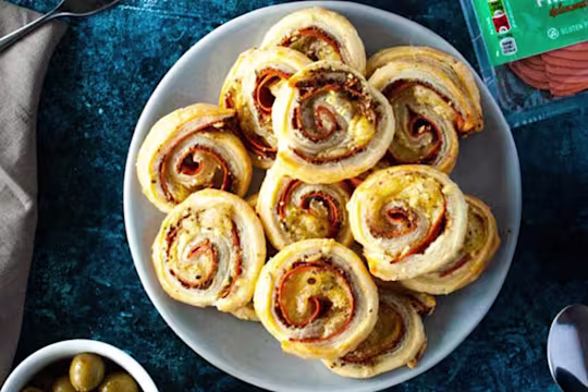 Vegan Quorn ham and cheese pin wheels served on a white plate with olive and nuts on the side.