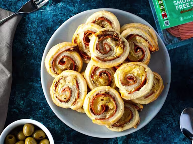 Vegan Quorn ham and cheese pin wheels served on a white plate with olive and nuts on the side.
