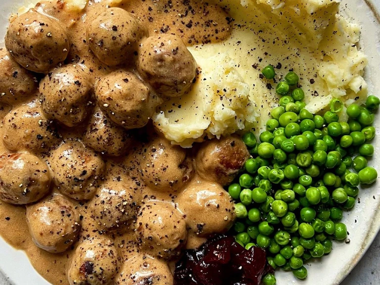 Quorn Meatballs and creamy gravy with mash, peas and jam, sprinkled with black pepper. 