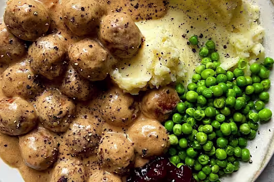 Quorn Meatballs and creamy gravy with mash, peas and jam, sprinkled with black pepper.
