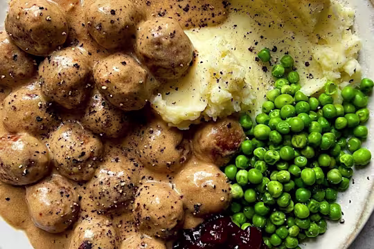 Quorn Meatballs and creamy gravy with mash, peas and jam, sprinkled with black pepper.