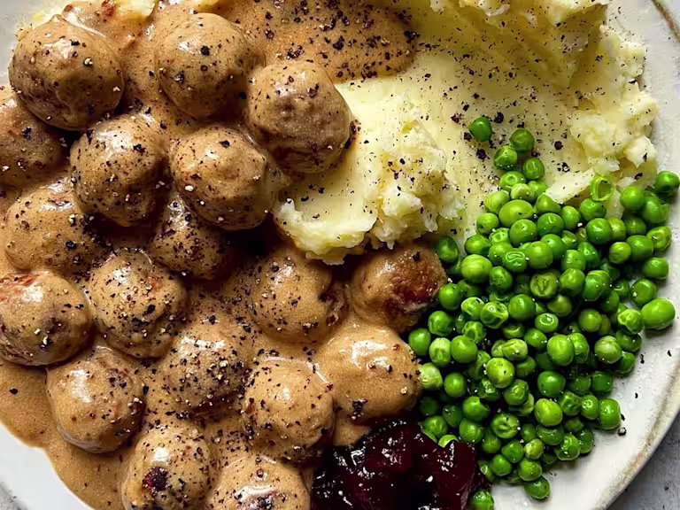 Quorn Meatballs and creamy gravy with mash, peas and jam, sprinkled with black pepper.