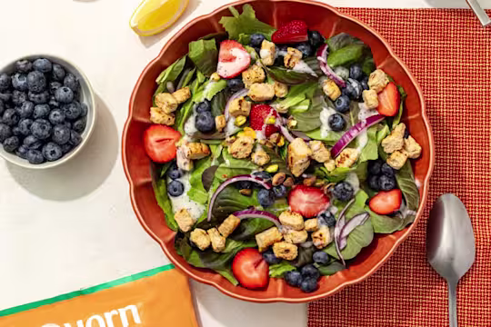 A bowl of lemon poppyseed salad with Quorn Chicken Pieces next to a bowl of blueberries and a spoon.