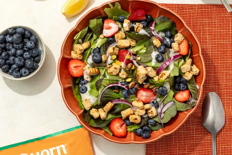 A bowl of lemon poppyseed salad with Quorn Chicken Pieces next to a bowl of blueberries and a spoon.