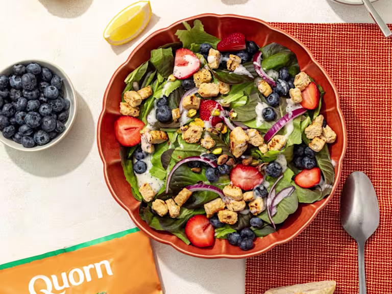A bowl of lemon poppyseed salad with Quorn Chicken Pieces next to a bowl of blueberries and a spoon.