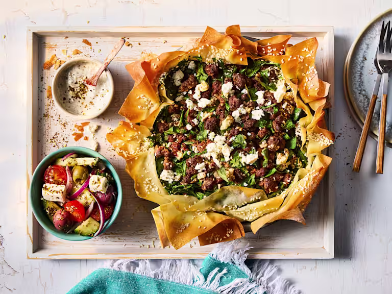 Feta and spinach Spanakopita on a wooden serving board with a yoghurt dip and side dish of vegetables.