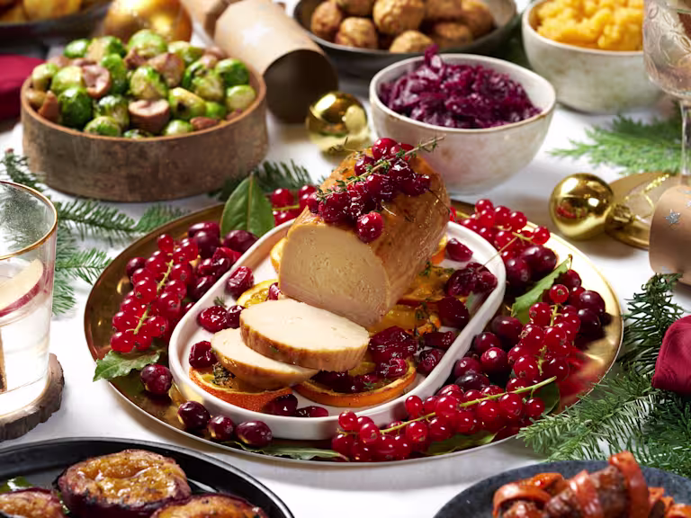 Cranberry and Orange Vegetarian Christmas roast made with a Quorn roast served on a dish, amongst a plate of cranberries and orange slides