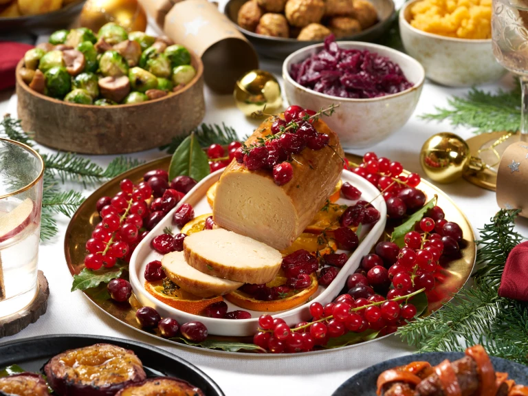 Cranberry and Orange Vegetarian Christmas roast made with a Quorn roast served on a dish, amongst a plate of cranberries and orange slides