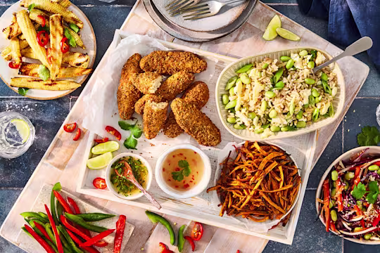 Serving tray featuring an assortment of sharing platter style dishes including Quorn Salt and Pepper Tenders, rice with edamame beans, chopped red and green pepper, baby corn with sliced chilli pepper and dishes and cutlery.