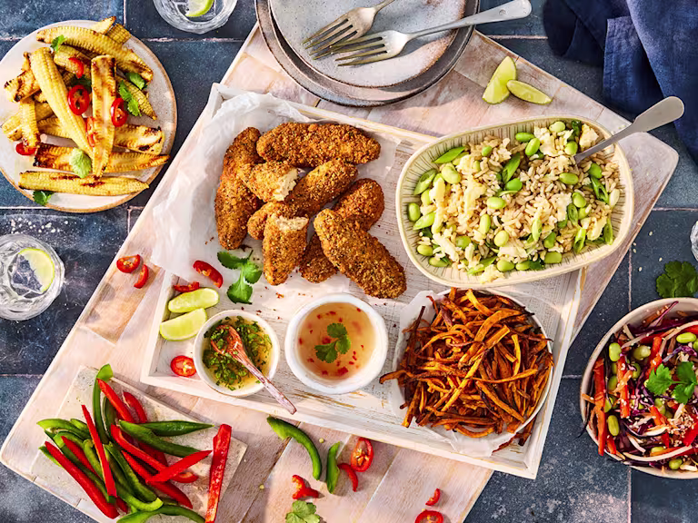 Serving tray featuring an assortment of sharing platter style dishes including Quorn Salt and Pepper Tenders, rice with edamame beans, chopped red and green pepper, baby corn with sliced chilli pepper and dishes and cutlery.