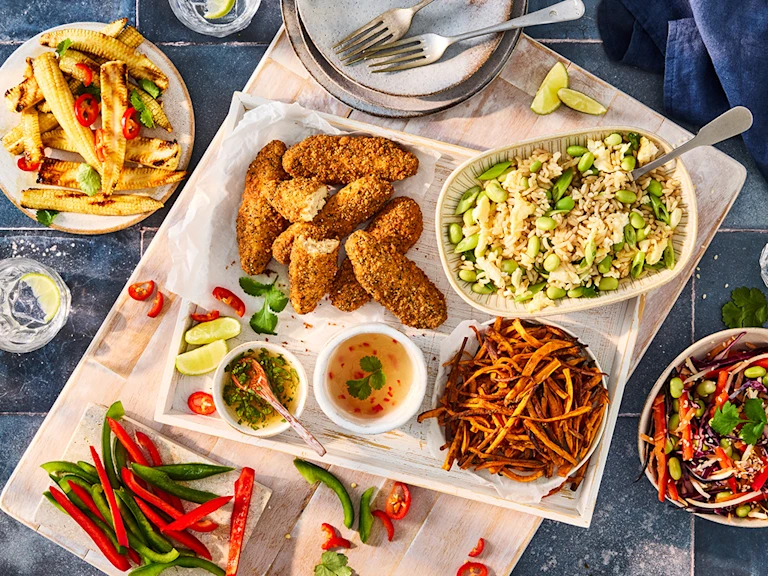Serving tray featuring an assortment of sharing platter style dishes including Quorn Salt and Pepper Tenders, rice with edamame beans, chopped red and green pepper, baby corn with sliced chilli pepper and dishes and cutlery.