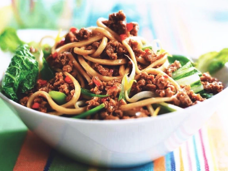 Egg noodles topped with Quorn Grounds, green onions, snow peas, and bok choy in a white bowl.