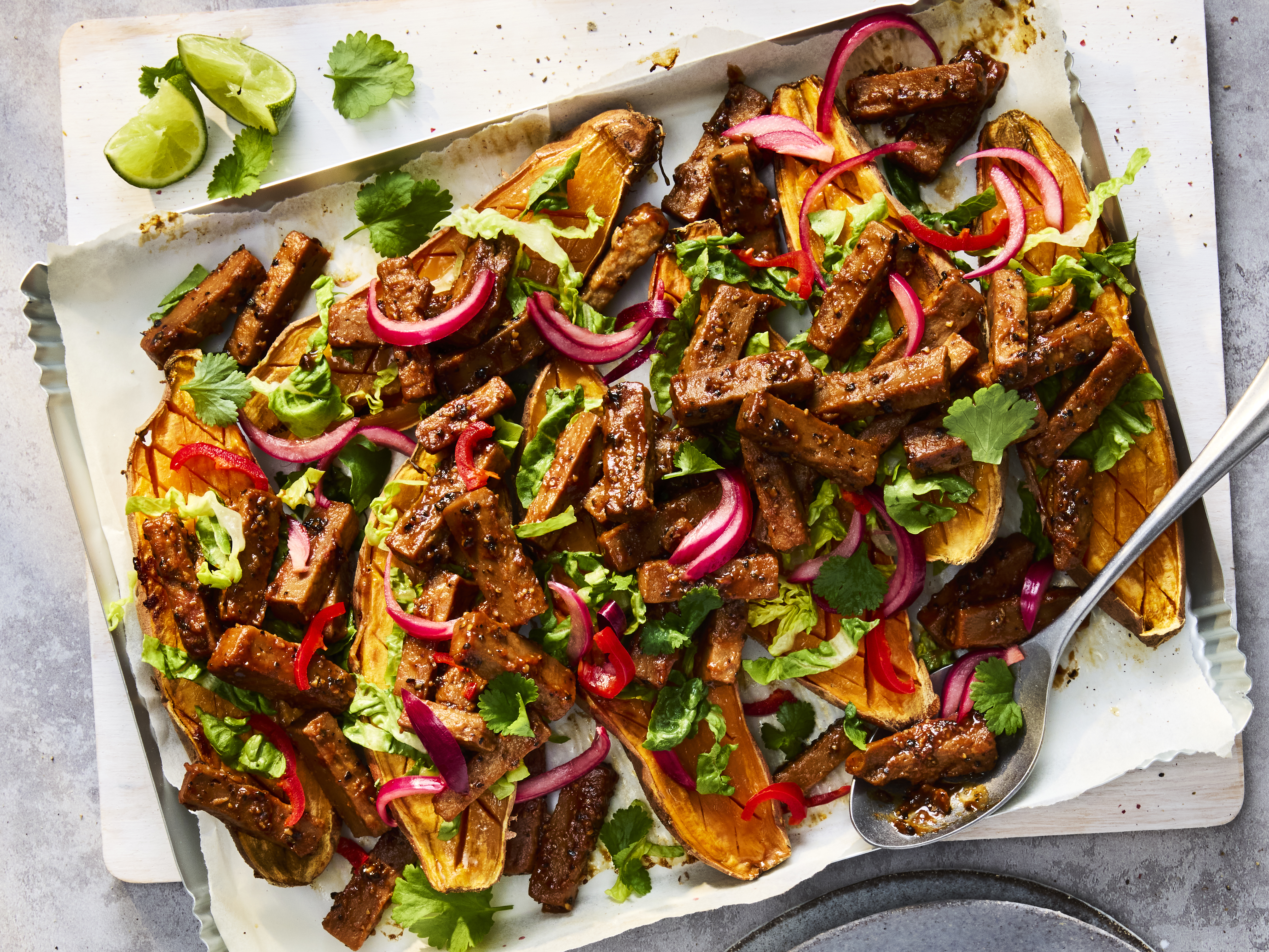 Sticky Szechuan Loaded Sweet Potatoes with Quorn Vegetarian Steak Strips and yoghurt, coriander and parsley on a white plate.