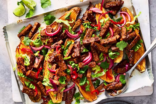 Sticky Szechuan Loaded Sweet Potatoes with Quorn Vegetarian Steak Strips and yoghurt, coriander and parsley on a white plate.
