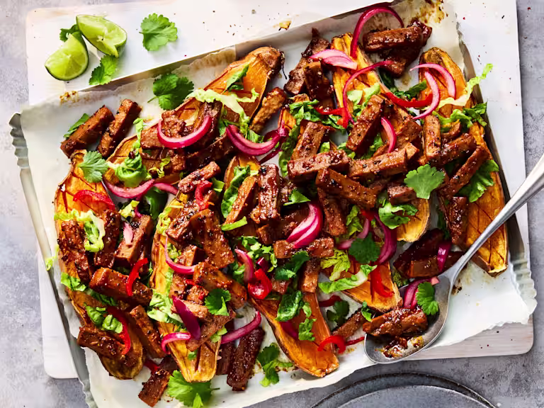 Sticky Szechuan Loaded Sweet Potatoes with Quorn Vegetarian Steak Strips and yoghurt, coriander and parsley on a white plate.