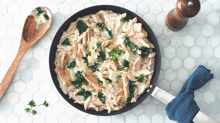 Gluten free recipe of Pasta Alfredo made with Quorn Roasted Sliced Fillets and penne pasta topped with kale served in a saucepan