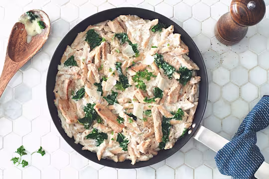 Gluten free recipe of Pasta Alfredo made with Quorn Roasted Sliced Fillets and penne pasta topped with kale served in a saucepan