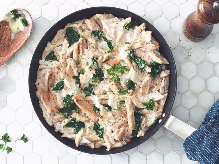 Gluten free recipe of Pasta Alfredo made with Quorn Roasted Sliced Fillets and penne pasta topped with kale served in a saucepan