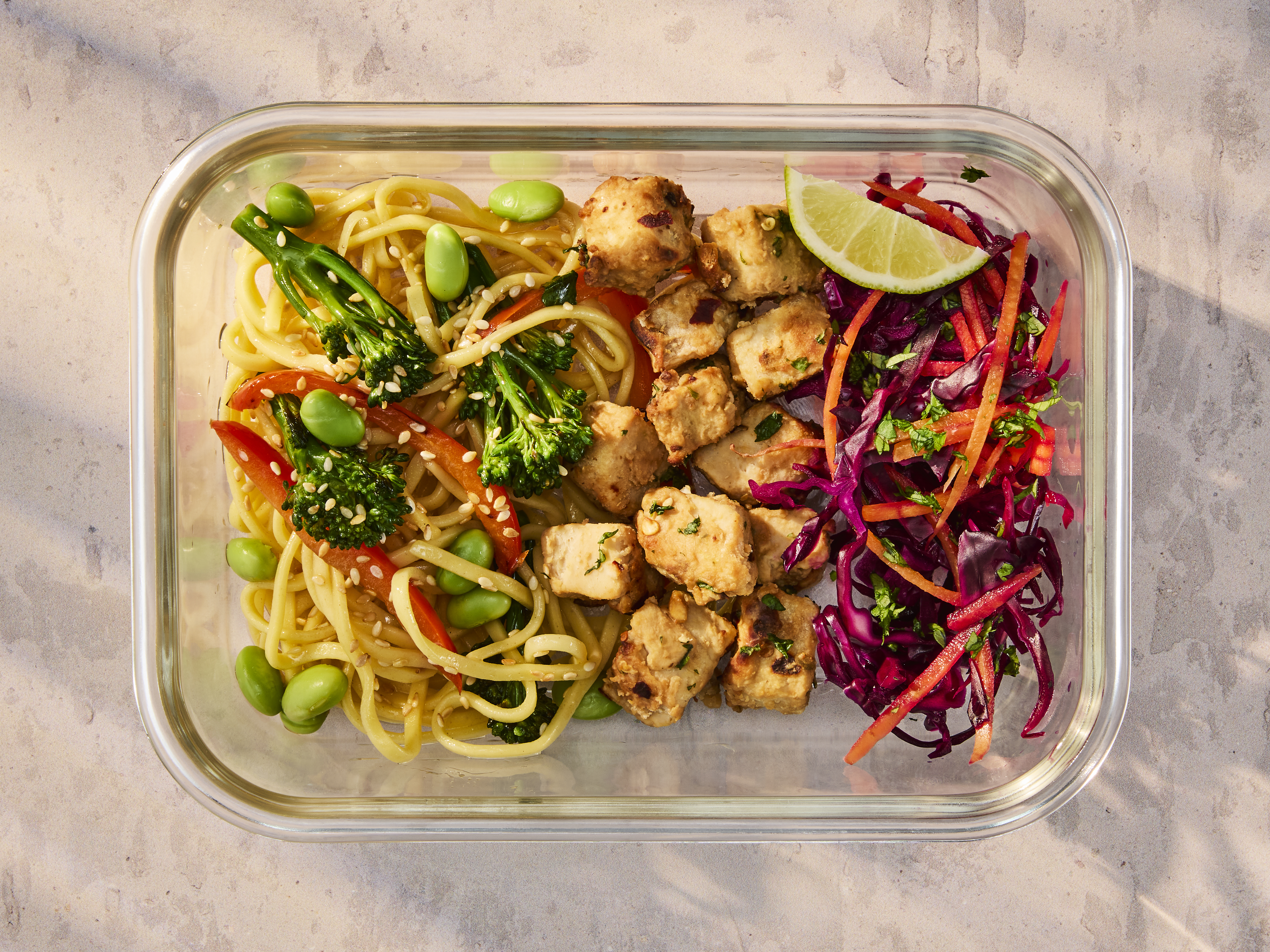 A glass meal prep container holding Vegetarian Satay Noodles with Quorn Pieces and a fresh cabbage slaw.